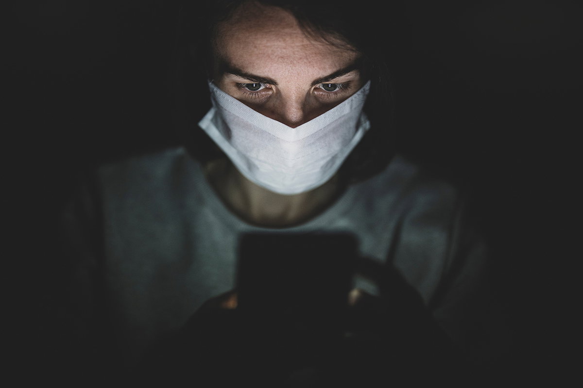 Person mit Mund- und Nasenschutz schaut auf Handy